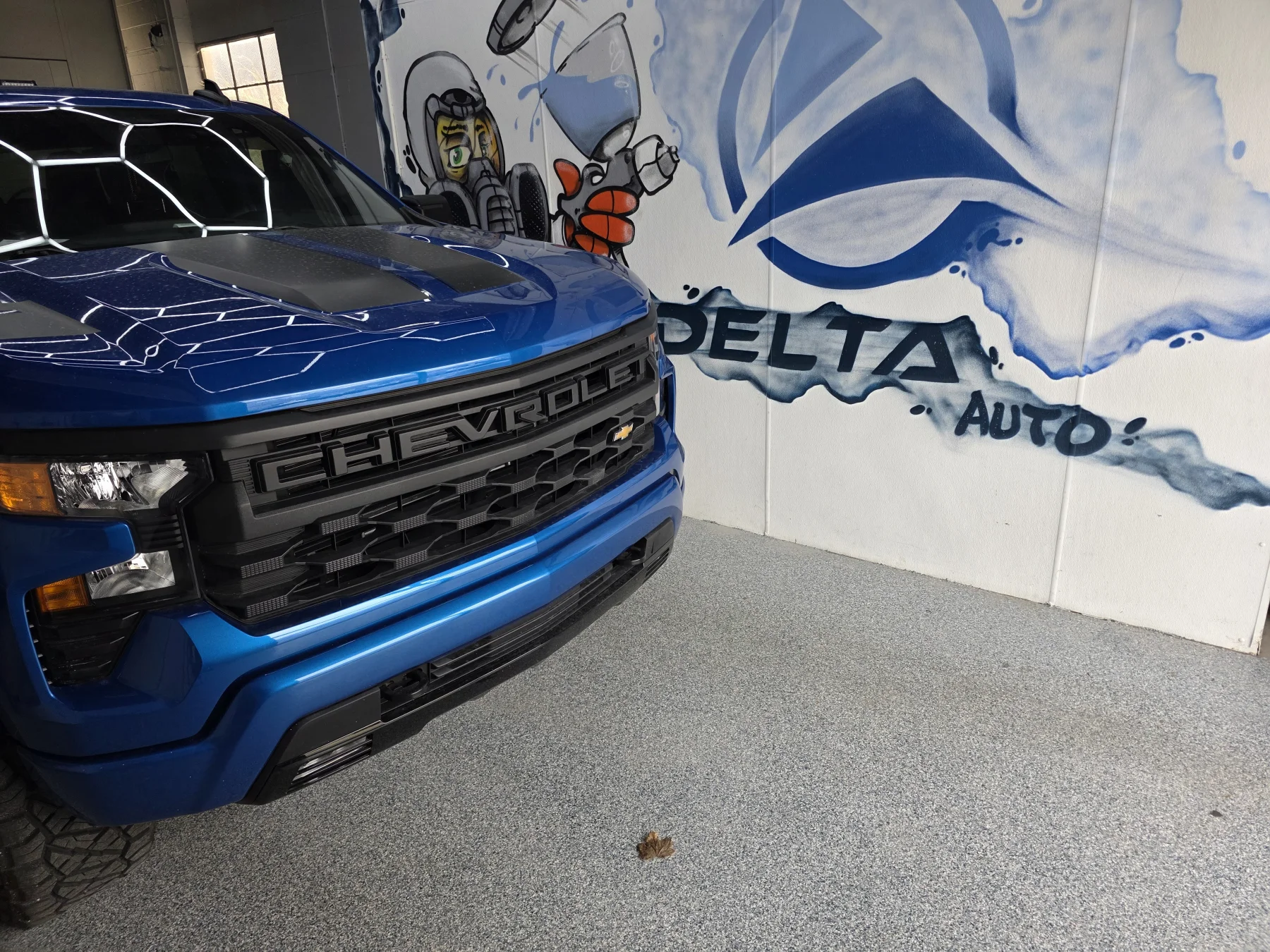 Blue Chevrolet truck beside the Delta Auto mural inside the shop